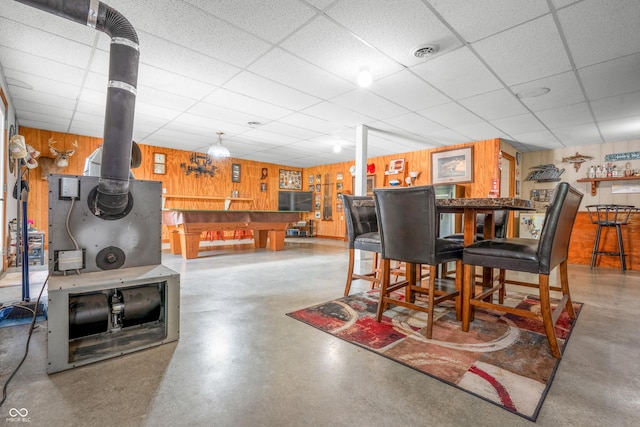 dining space featuring concrete flooring, wood walls, a paneled ceiling, and a dry bar