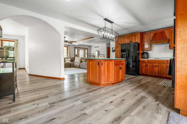 kitchen with black appliances, premium range hood, arched walkways, and light wood finished floors