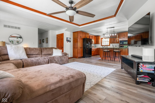 living area featuring a ceiling fan, light wood-type flooring, a tray ceiling, and ornamental molding