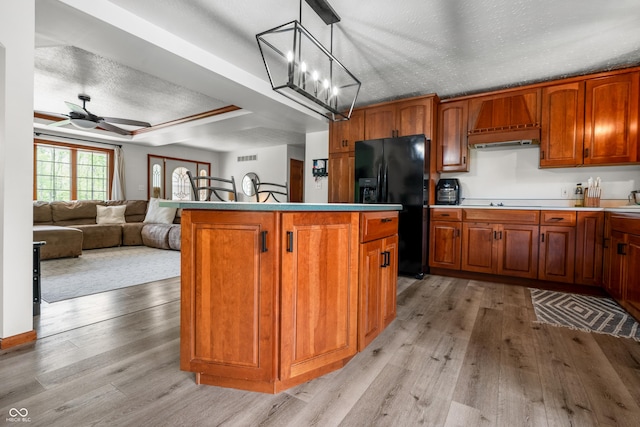 kitchen featuring black fridge, light wood-style floors, a ceiling fan, brown cabinetry, and a textured ceiling