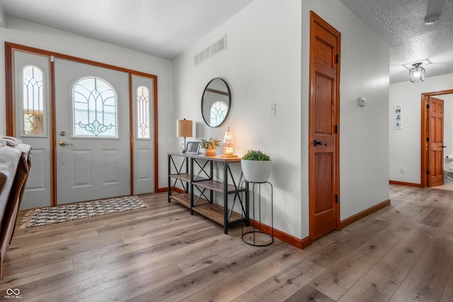 entryway with a textured ceiling, wood-type flooring, and baseboards