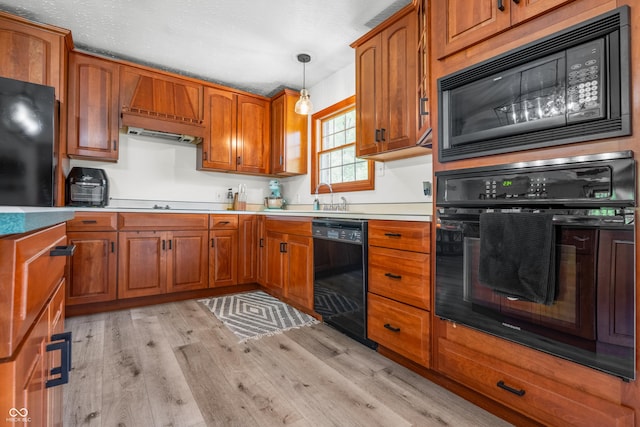 kitchen with black appliances, a sink, light wood finished floors, brown cabinetry, and pendant lighting