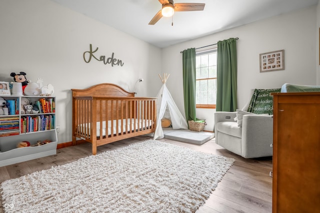 bedroom with a crib, wood finished floors, and a ceiling fan