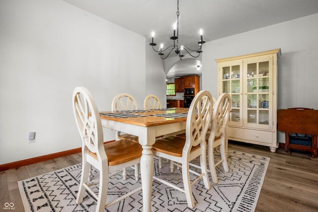 dining space featuring a chandelier, wood finished floors, arched walkways, and baseboards