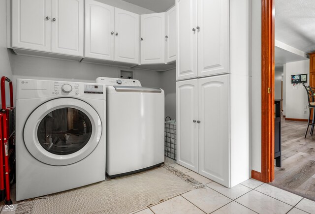 laundry area with cabinet space, washing machine and dryer, baseboards, and light tile patterned floors