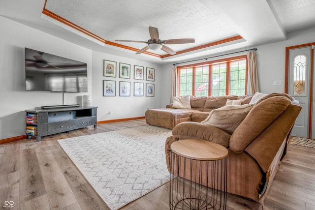 living room featuring a raised ceiling, healthy amount of natural light, a ceiling fan, and a textured ceiling