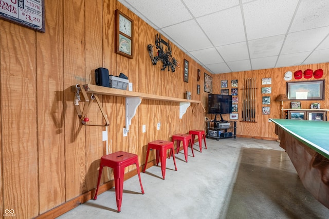 rec room featuring wooden walls, concrete flooring, and a paneled ceiling