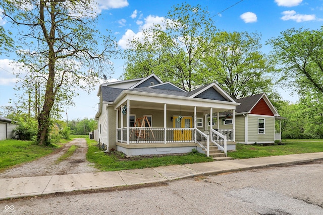 view of front of house featuring a porch, dirt driveway, and a shingled roof
