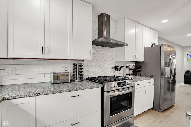 kitchen featuring appliances with stainless steel finishes, wall chimney exhaust hood, white cabinetry, light stone countertops, and recessed lighting