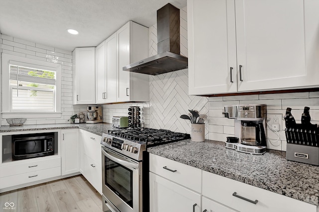 kitchen with wall chimney exhaust hood, gas range, tasteful backsplash, light stone counters, and white cabinetry