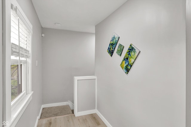 hallway featuring plenty of natural light, light wood-style flooring, baseboards, and an upstairs landing