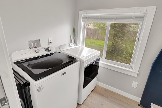 laundry room featuring washing machine and dryer, baseboards, and light wood finished floors