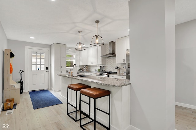 kitchen featuring wall chimney exhaust hood, stainless steel gas range oven, light stone counters, a kitchen bar, and backsplash