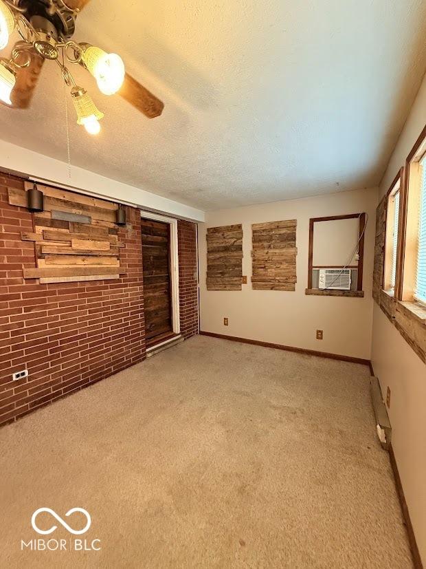 empty room featuring light carpet, brick wall, baseboards, cooling unit, and a textured ceiling