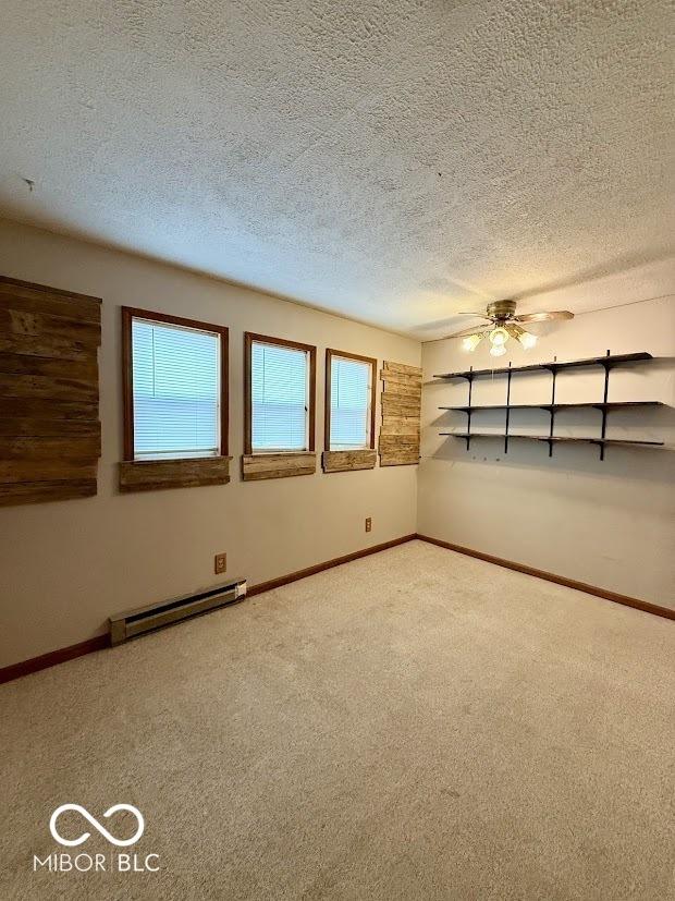 empty room featuring a baseboard heating unit, carpet flooring, baseboards, a textured ceiling, and ceiling fan