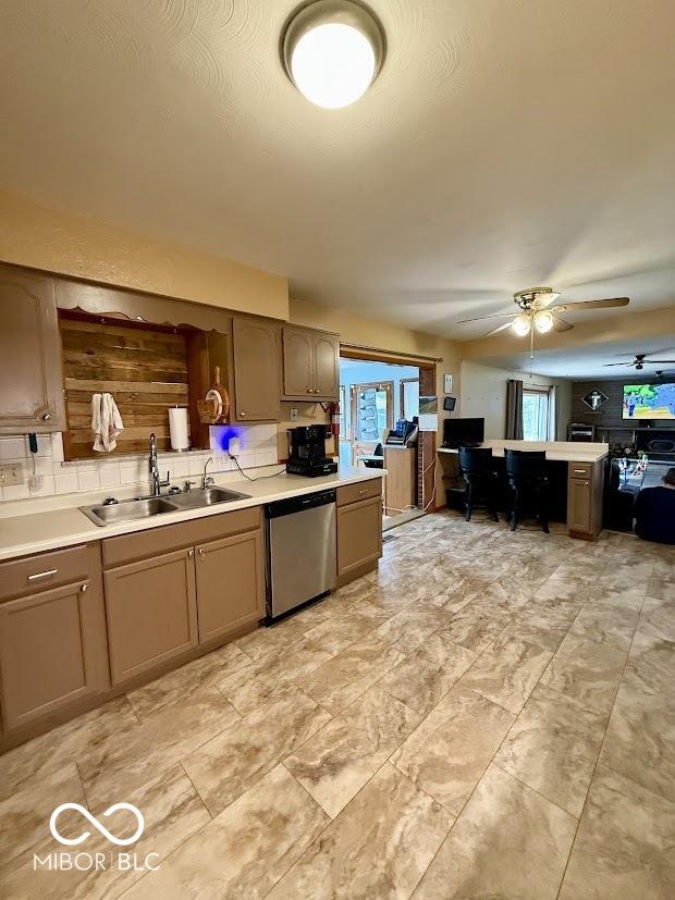kitchen featuring dishwasher, a sink, ceiling fan, backsplash, and light countertops