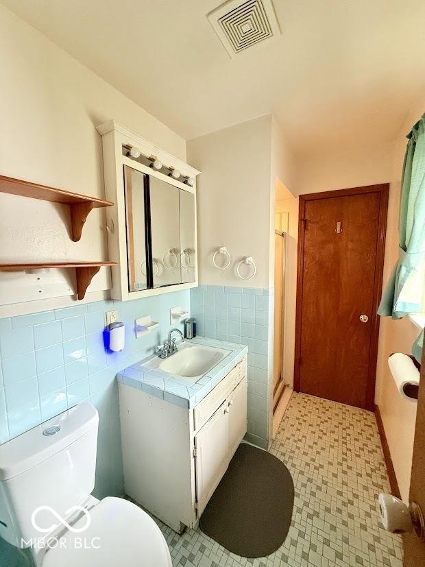 bathroom featuring tile walls, vanity, toilet, and a stall shower