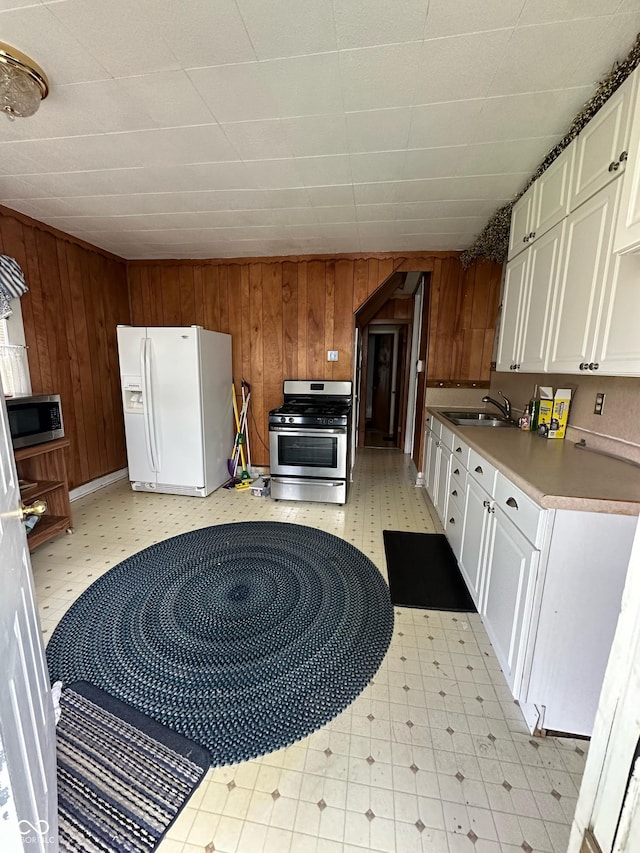 803 W 12th St, Anderson, IN 46016 - kitchen featuring appliances with stainless steel finishes, a sink, wood walls, white cabinets, and light floors