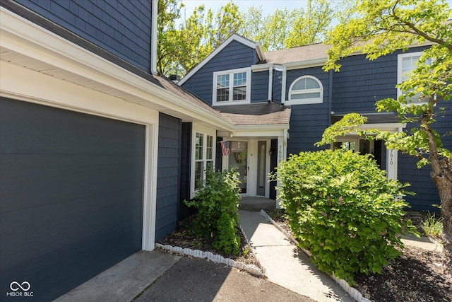doorway to property with a garage, roof with shingles, and asphalt driveway