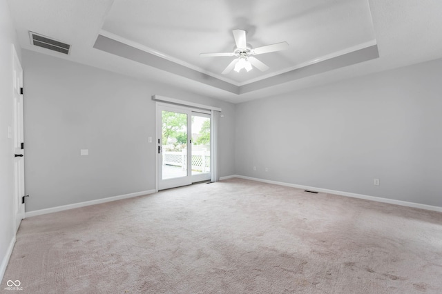 carpeted spare room featuring a tray ceiling, ceiling fan, crown molding, and baseboards