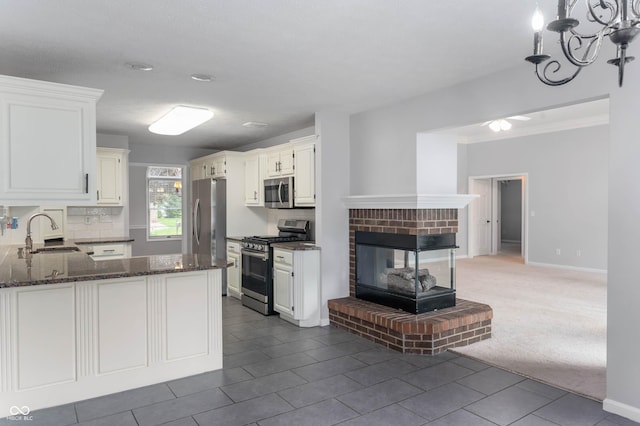 kitchen featuring stainless steel appliances, a sink, white cabinetry, and dark stone counters