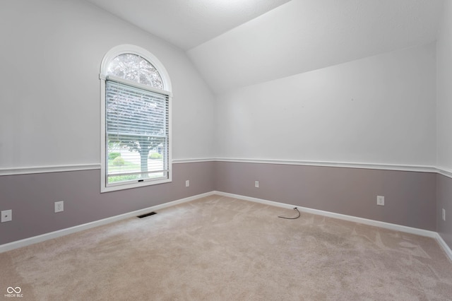 carpeted spare room featuring vaulted ceiling and baseboards