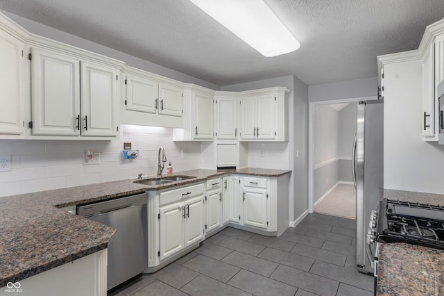 kitchen with appliances with stainless steel finishes, a sink, white cabinetry, backsplash, and a textured ceiling