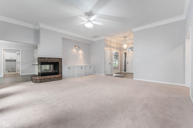 unfurnished living room featuring a ceiling fan, crown molding, a brick fireplace, carpet floors, and baseboards