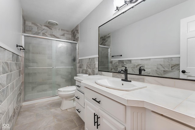 full bath with a shower stall, vanity, toilet, and tile walls