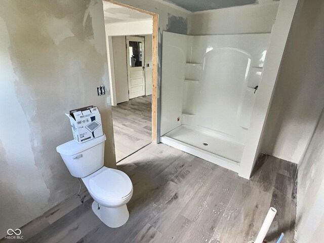 bathroom with a stall shower, toilet, and wood finished floors