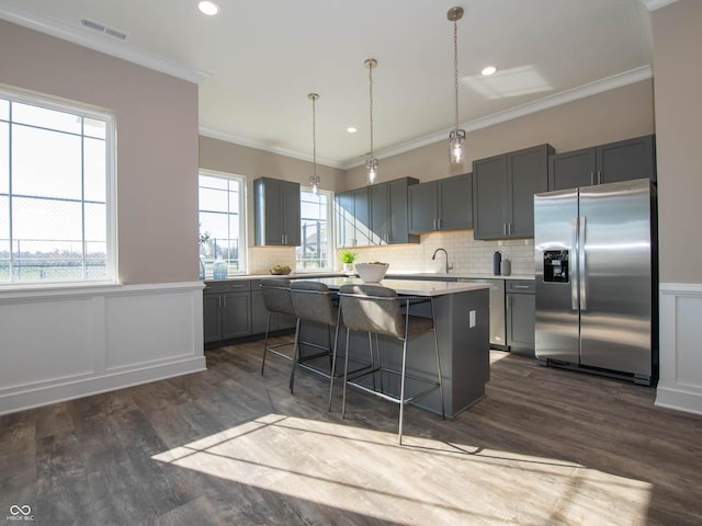 kitchen with appliances with stainless steel finishes, a center island, dark wood finished floors, a kitchen breakfast bar, and a wainscoted wall