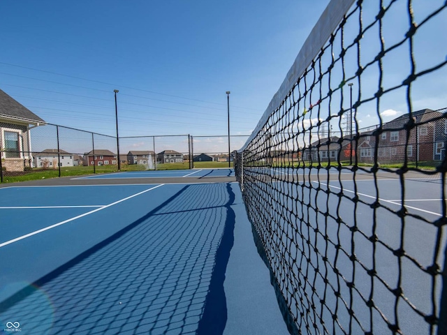 view of tennis court featuring fence and a residential view