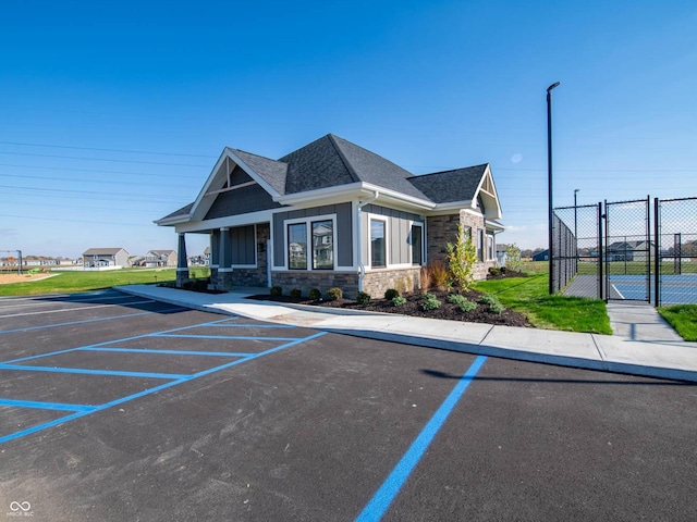 view of front of property with stone siding, uncovered parking, fence, a shingled roof, and board and batten siding