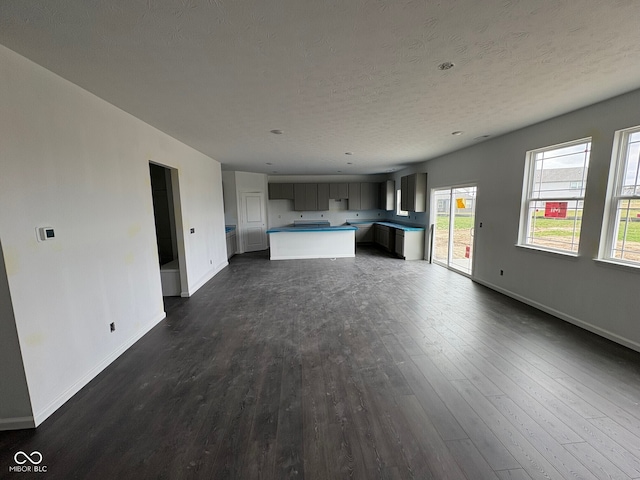 unfurnished living room featuring baseboards, dark wood-style flooring, a textured ceiling, and healthy amount of natural light