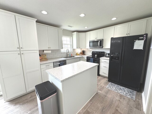 kitchen with black appliances, a sink, light wood finished floors, tasteful backsplash, and white cabinetry