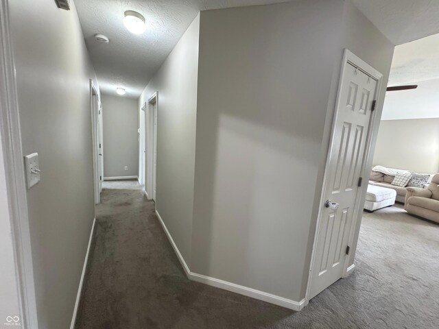hallway with carpet floors, baseboards, and a textured ceiling