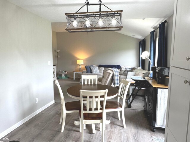 dining area featuring wood finished floors, lofted ceiling, and baseboards