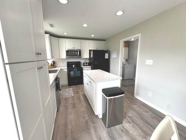 kitchen with black appliances, light wood-type flooring, separate washer and dryer, a kitchen island, and white cabinetry