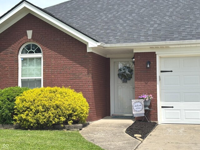 property entrance with a shingled roof, brick siding, and a garage