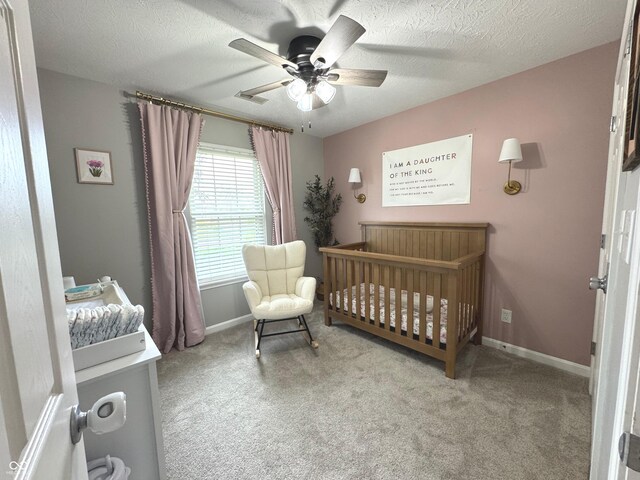carpeted bedroom featuring a crib, baseboards, a ceiling fan, and a textured ceiling