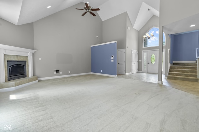 unfurnished living room featuring high vaulted ceiling, carpet floors, a tiled fireplace, stairs, and a ceiling fan