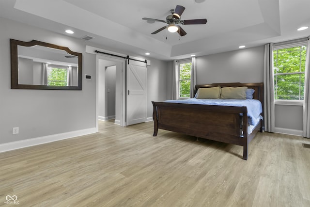 bedroom featuring a barn door, a raised ceiling, baseboards, light wood-type flooring, and recessed lighting