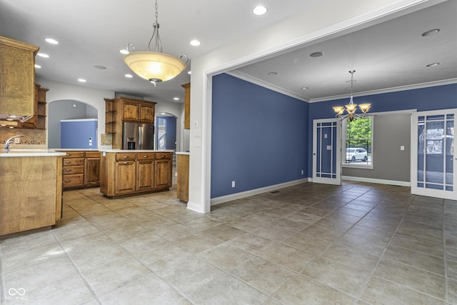 kitchen featuring stainless steel refrigerator with ice dispenser, light countertops, backsplash, brown cabinetry, and a chandelier