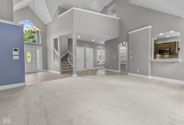 unfurnished living room with high vaulted ceiling, light carpet, stairs, a chandelier, and light tile patterned floors