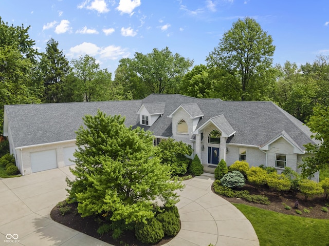 view of front of property with a shingled roof, driveway, an attached garage, brick siding, and view of wooded area