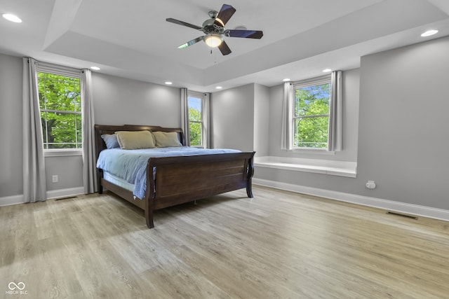 bedroom with baseboards, light wood-type flooring, a raised ceiling, recessed lighting, and ceiling fan