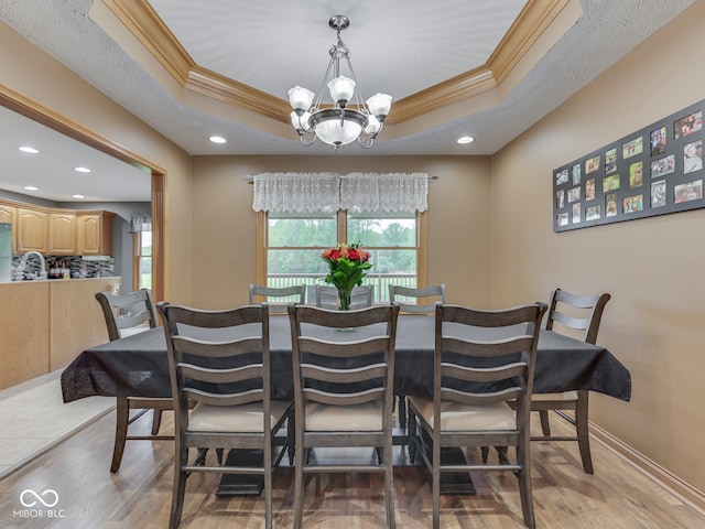 dining space with a chandelier, ornamental molding, light wood-type flooring, a tray ceiling, and recessed lighting