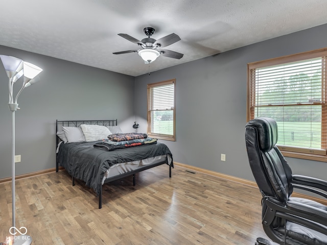 bedroom featuring light wood-type flooring, baseboards, a desk, and ceiling fan