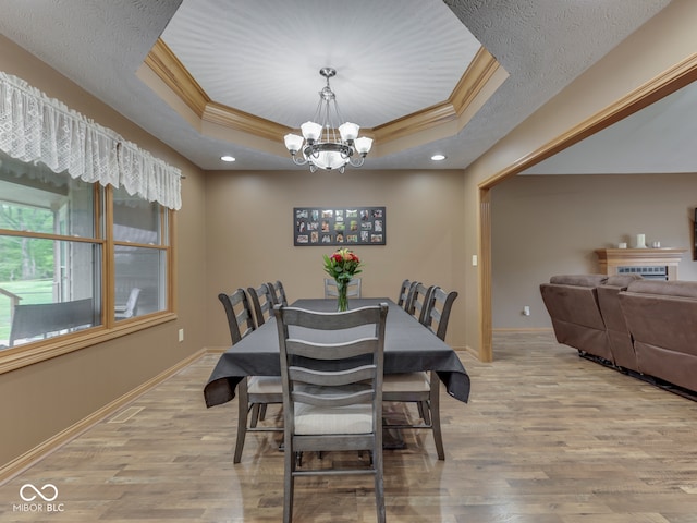 dining space featuring a tray ceiling, a chandelier, light wood-type flooring, baseboards, and ornamental molding