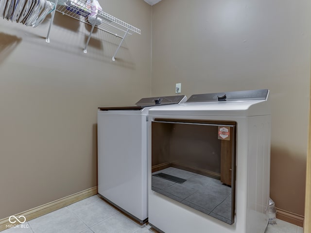 laundry area featuring separate washer and dryer, light tile patterned floors, and baseboards